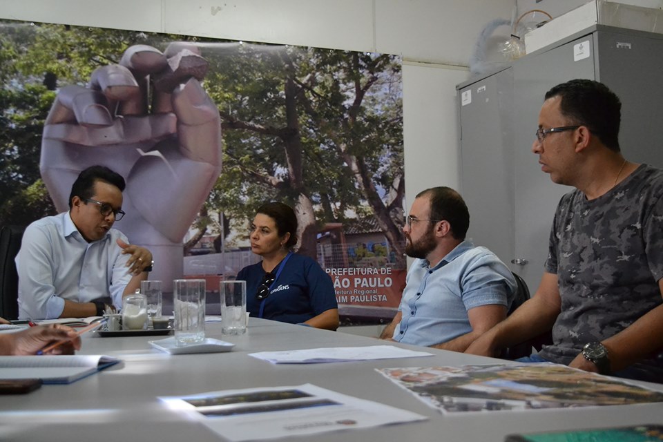 Foto tirada durante a reunião. Ela apresenta quatro pessoas – três homens e uma mulher – conversando. O subprefeito, Gilmar Souza Santos, é um deles. 